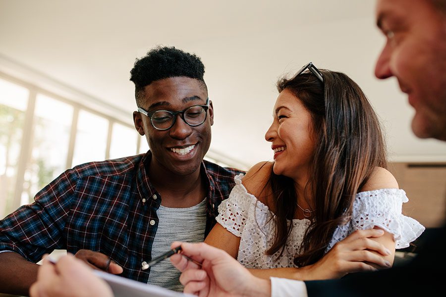 About Our Agency - View of Cheerful Young Couple Sitting in an Insurance Agents Office Being Advised on an Insurance Policy